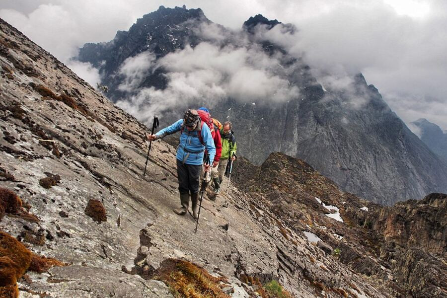 Climbers crossing a steep, rocky ridge in the clouds