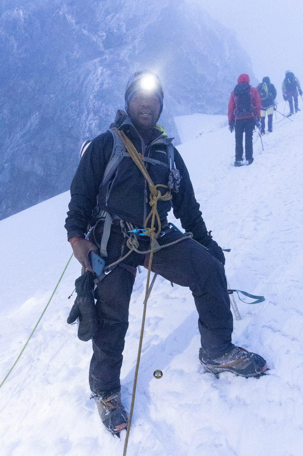 Roped climber with headlamp on a snowy slope