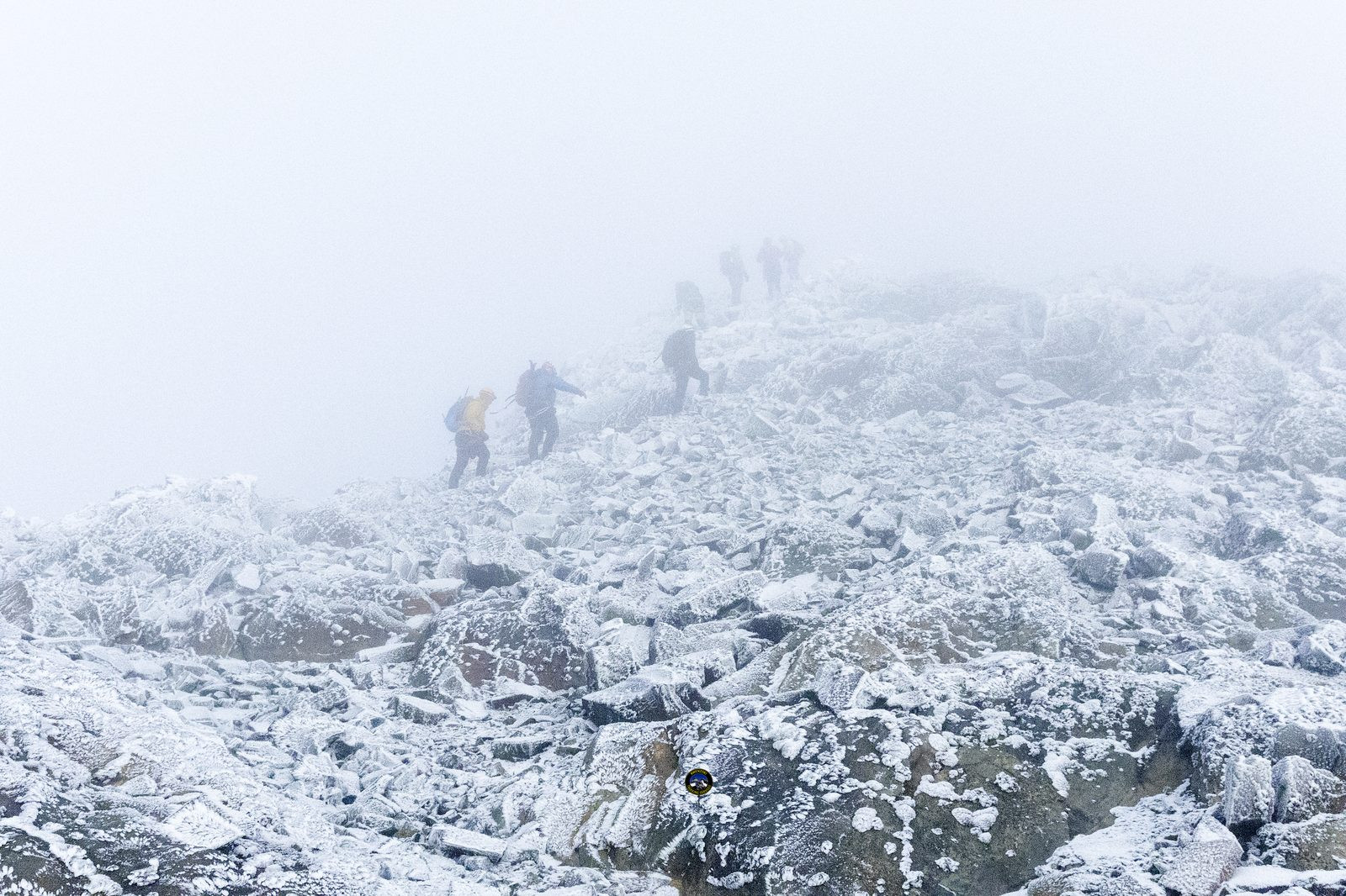 Climbers ascending a snowy rocky ridge in thick fog