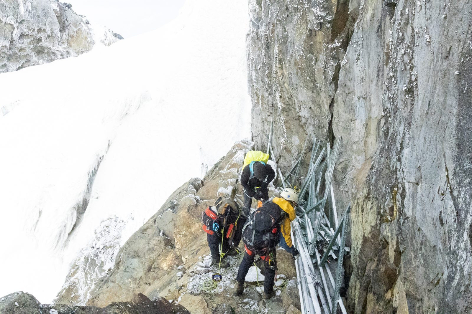Climbers on a narrow rock ledge with metal scaffolding