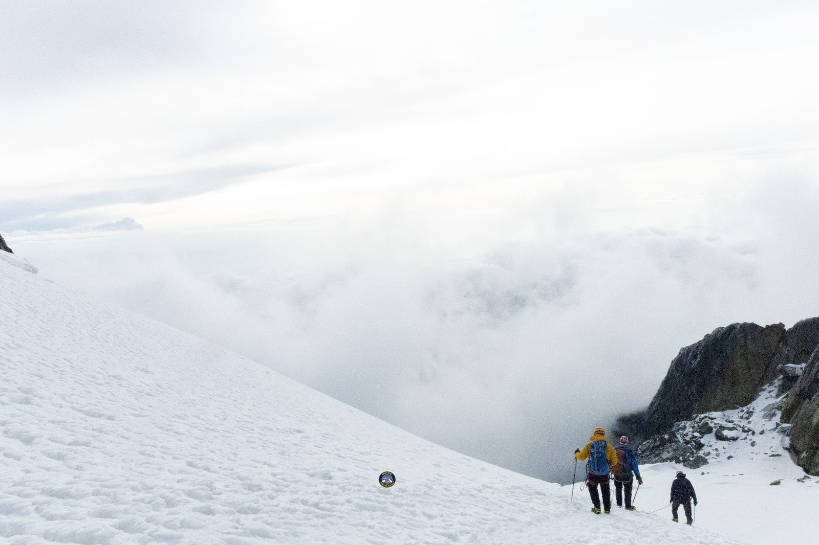 Climbers descending a snow slope above the clouds