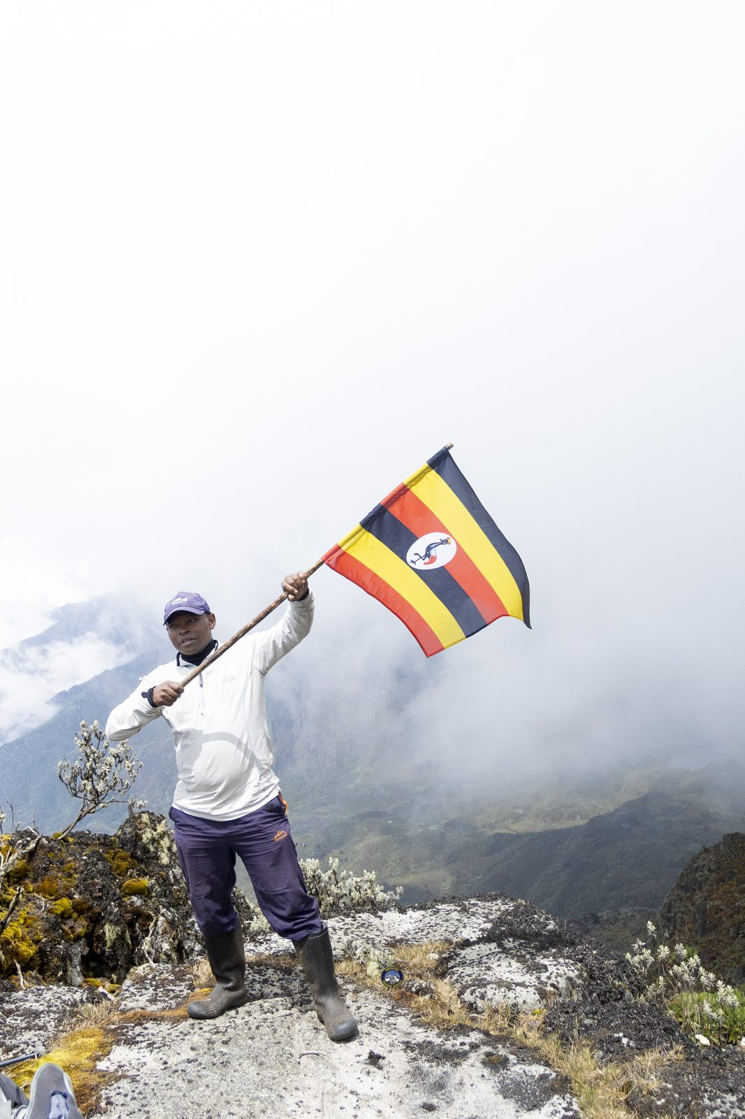 Guide waving the Uganda flag from a mountain viewpoint